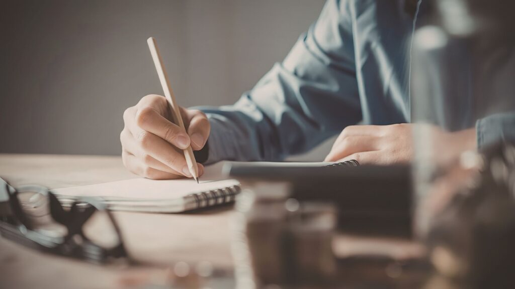 ノートに鉛筆で書きながら考えている人の手元